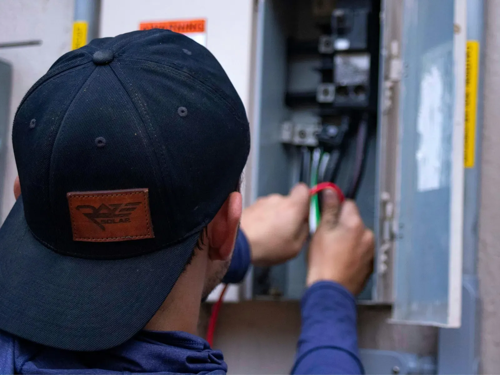 An electrician in a cap working inside an open residential breaker panel